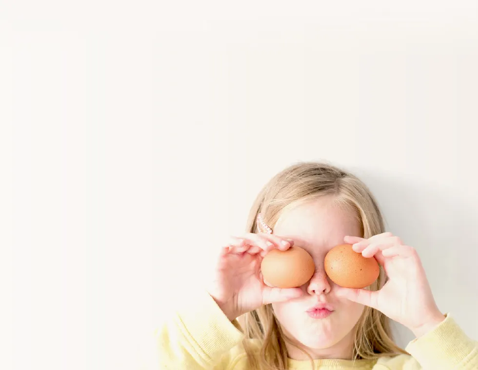 Young girl playfully holding two eggs over her eyes